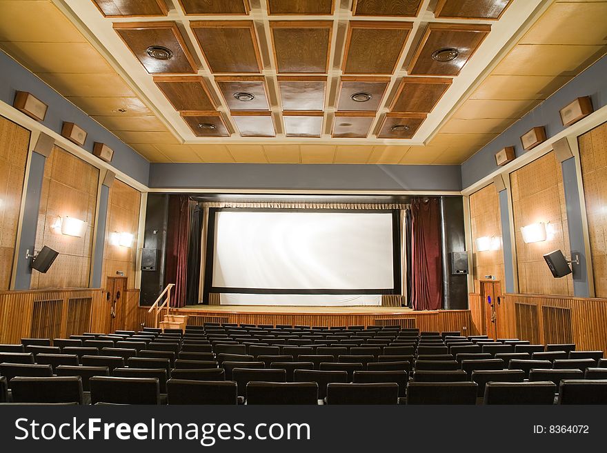 Empty old retro style cinema auditorium with line of chairs and stage with silver screen. Ready for adding your own picture. Empty old retro style cinema auditorium with line of chairs and stage with silver screen. Ready for adding your own picture.