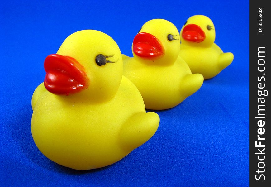 Three small rubber duckies in a row on a blue background. Three small rubber duckies in a row on a blue background