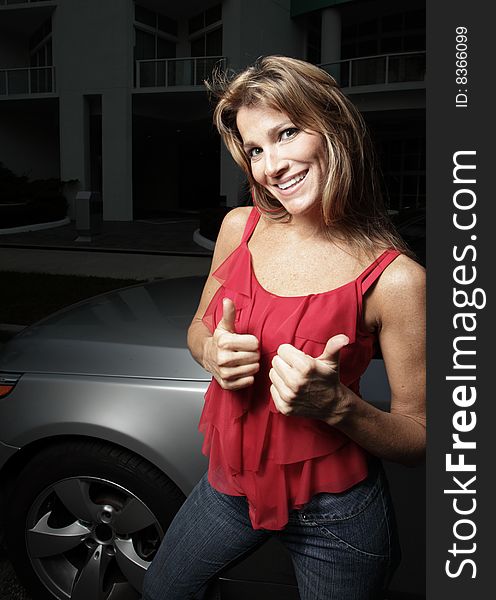 Woman posing by a luxury automobile and displaying a thumbs-up gesture. Woman posing by a luxury automobile and displaying a thumbs-up gesture