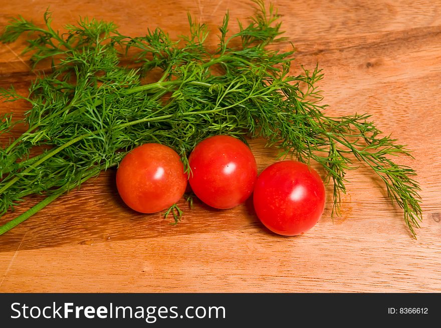 Three red tomatoes  and dill on a wooden kitchen board. Three red tomatoes  and dill on a wooden kitchen board