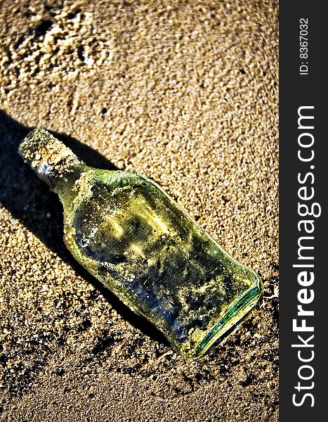 Green glass bottle in the sand. Green glass bottle in the sand.