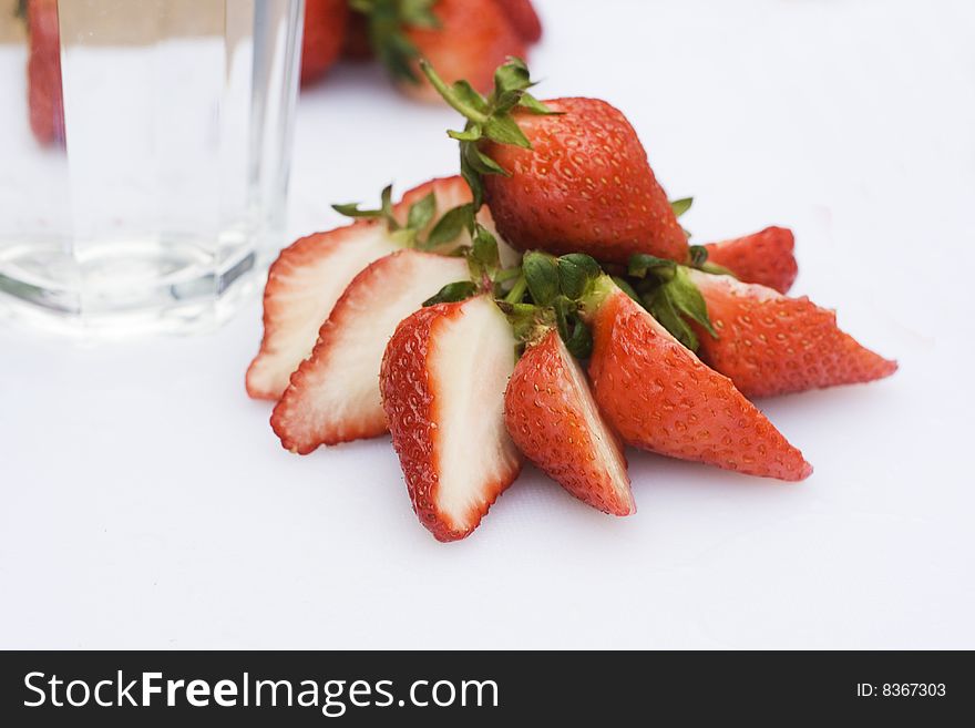 Some Strawberries have been cut in half and put into a circle. There are some whole strawberries in the background. There's also a glass of water. Some Strawberries have been cut in half and put into a circle. There are some whole strawberries in the background. There's also a glass of water