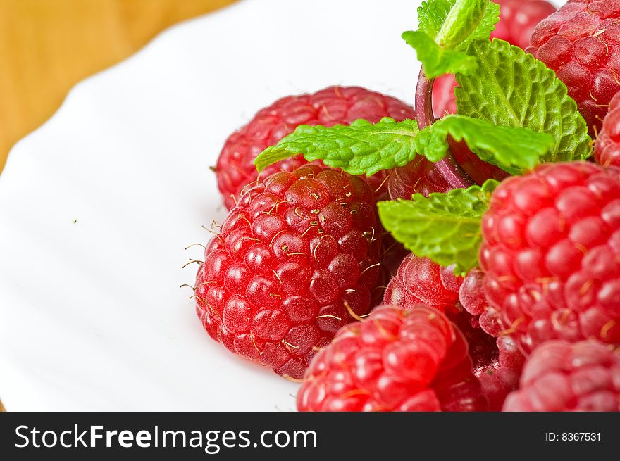 Fresh ripe rasberry and fresh mint leaves close-up on white porcelain plate. Fresh ripe rasberry and fresh mint leaves close-up on white porcelain plate