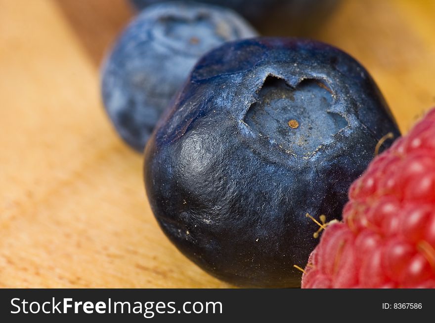 A couple of fresh ripe rasberry and blueberry on the wooden plate. A couple of fresh ripe rasberry and blueberry on the wooden plate