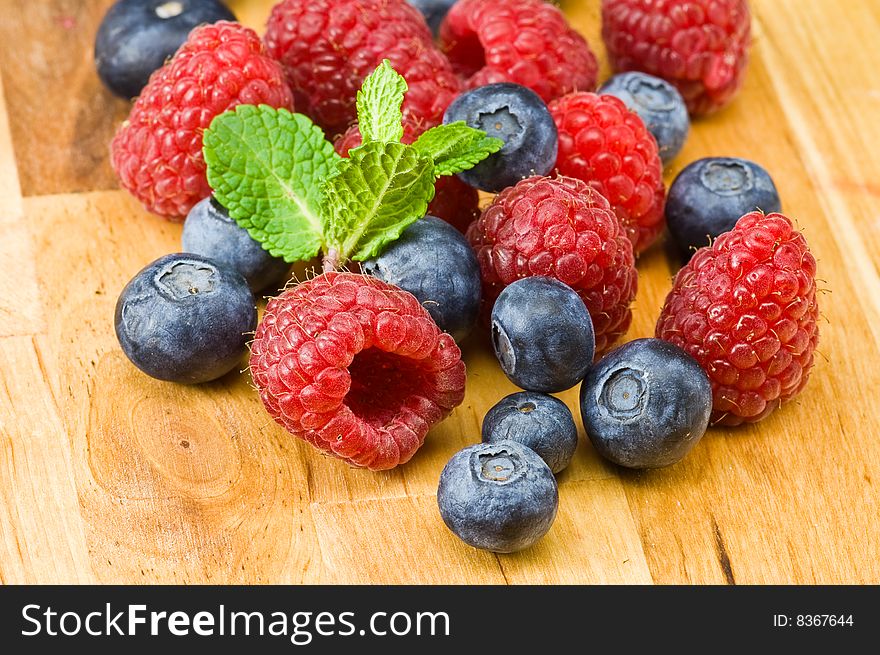 Fresh ripe raspberry and blueberry with green mint leaves on wooden plate. Fresh ripe raspberry and blueberry with green mint leaves on wooden plate