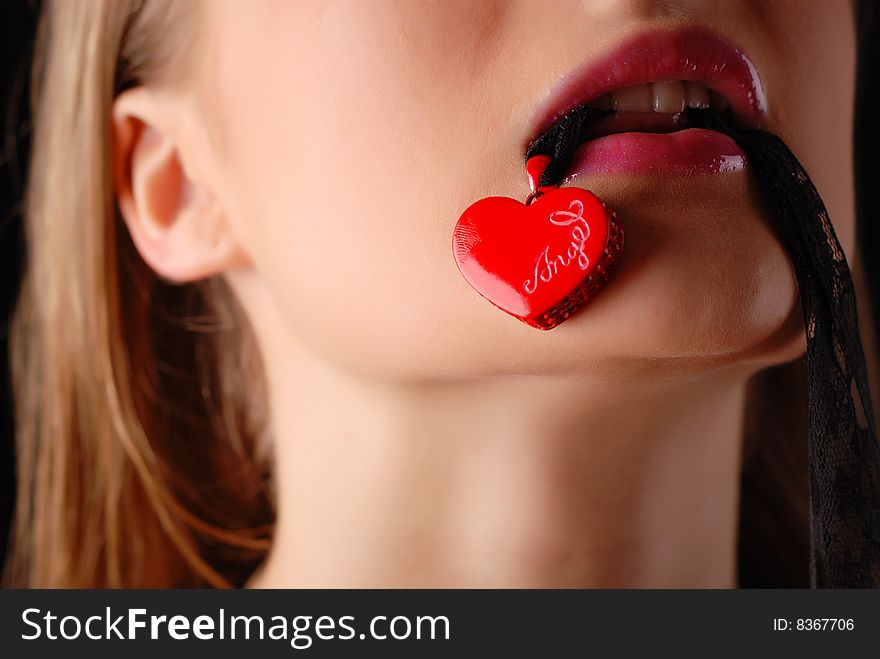 Young beautiful woman holding red heart in her mouth. Young beautiful woman holding red heart in her mouth