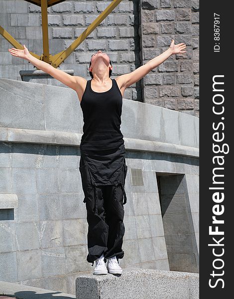 Beautiful brunette stands on stone block with raised hands