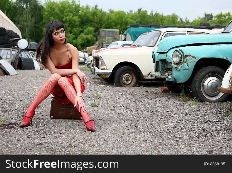 Girl sit atop vintage suitcase beside retro cars. Girl sit atop vintage suitcase beside retro cars