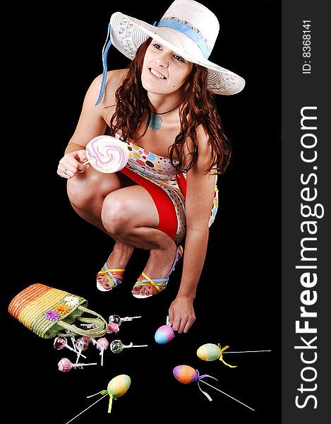 Lovely woman in an colorful dress and a white hat with eastern
eggs on the floor, over black background. Lovely woman in an colorful dress and a white hat with eastern
eggs on the floor, over black background.