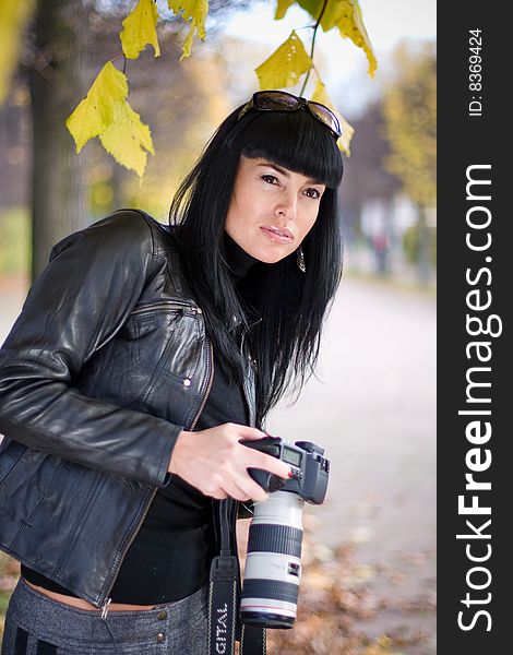 Portrait of beautiful fashion brunette girl in the park, holding photocamera