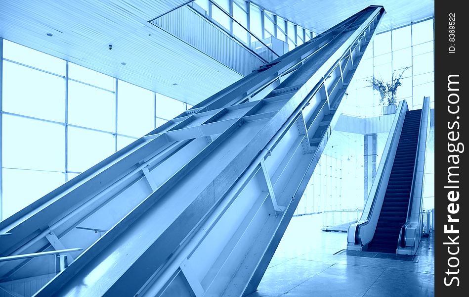 Glass hall with escalator on blue tones