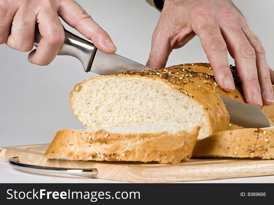 A man with long knife slicing through a large loaf of bread. A man with long knife slicing through a large loaf of bread.