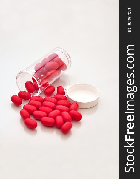 Small vile of pills spilled on top of a whit shiny table with red  pills. Small vile of pills spilled on top of a whit shiny table with red  pills.