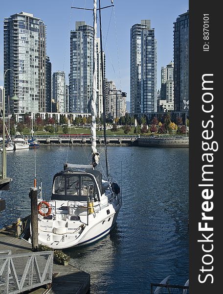 White sailboat docked in the harbor with the city skyline in the background.