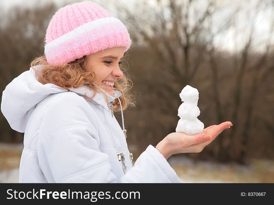 Young beauty girl outdoor in winter holds small snowman in hands. Young beauty girl outdoor in winter holds small snowman in hands