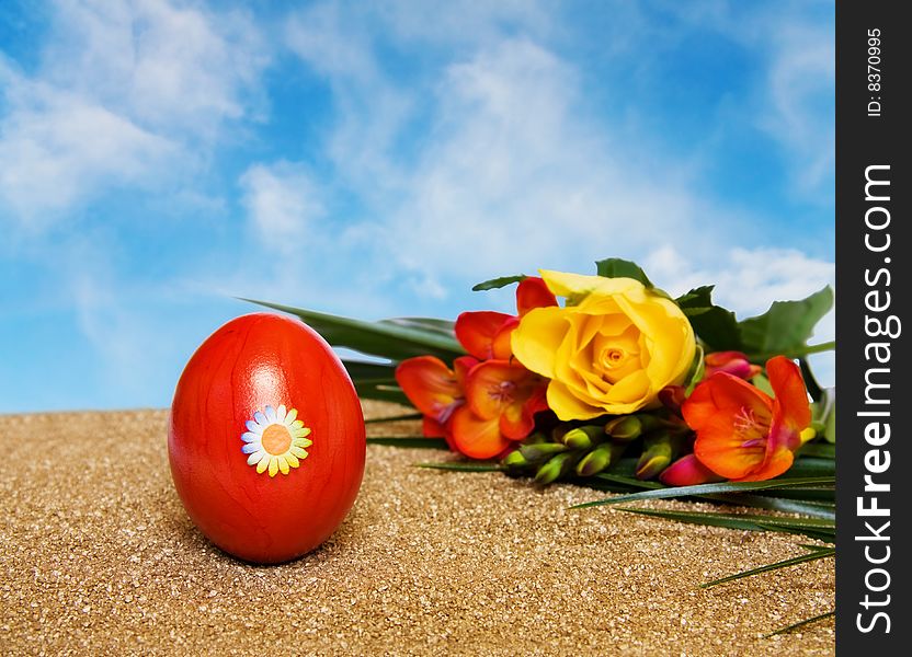 Easter spring celebration with red decorated egg, yellow rose and freesia flowers over golden sand and clear blue sky. Room for your text. Easter spring celebration with red decorated egg, yellow rose and freesia flowers over golden sand and clear blue sky. Room for your text.