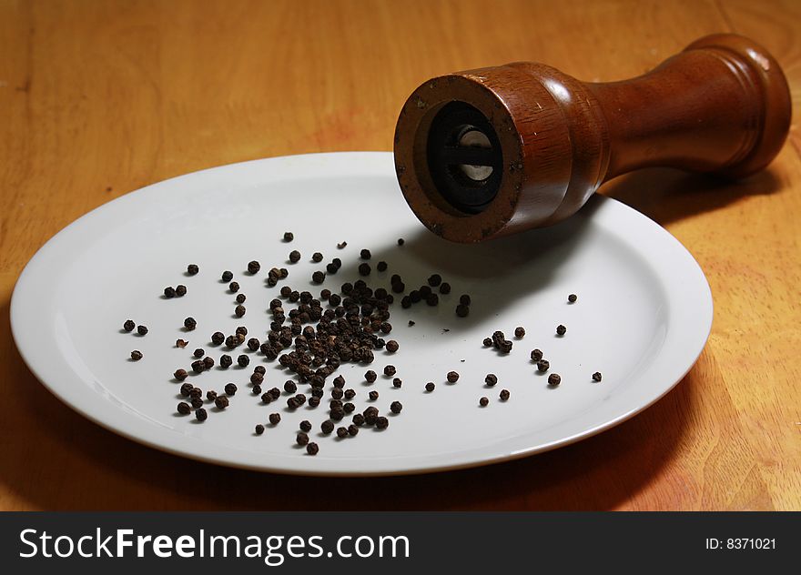 Close up of black peppercorns scattered on the plate and pepper mill. Close up of black peppercorns scattered on the plate and pepper mill