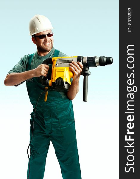 Smiled workman in helmet, black glasses and overalls hold perforator in his hands and drilled over white background. Smiled workman in helmet, black glasses and overalls hold perforator in his hands and drilled over white background