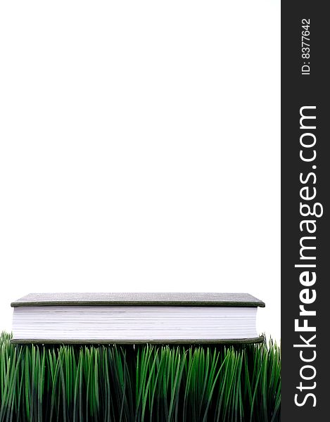 Green hardcover book sitting on grass with a white background. Green hardcover book sitting on grass with a white background