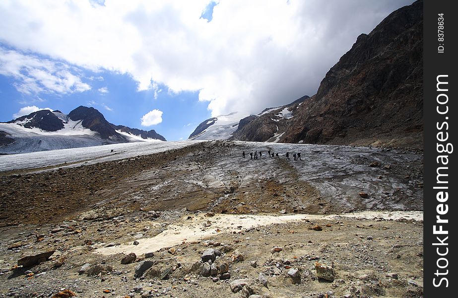 Trekkers and high mountains landscape in the alps during summer. The remains of a big glacier illustrating the global warming.
