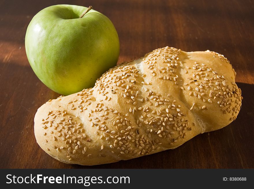 A bread loaf on a wooden table, with a green apple. A bread loaf on a wooden table, with a green apple