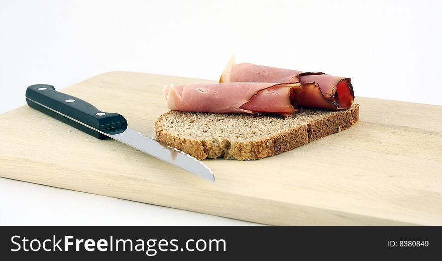 A slice of bread with ham presented on a wooden plate. A slice of bread with ham presented on a wooden plate