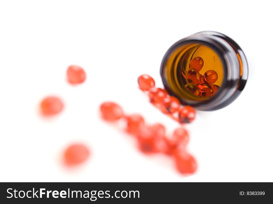 Glass bottle with red pills on white background