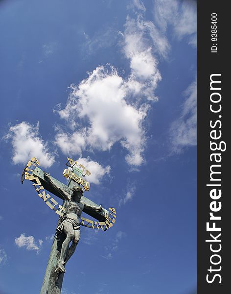 A large sculpted Jesus crucifix with gilded lettering and the blue cloudy sky in the background. On the Charles Bridge (Karlov Most) in Prague, Czech Republic. A large sculpted Jesus crucifix with gilded lettering and the blue cloudy sky in the background. On the Charles Bridge (Karlov Most) in Prague, Czech Republic.