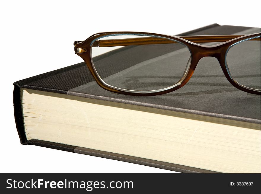 A close up partial view of a hardback book with a pair of reading glasses on top. A close up partial view of a hardback book with a pair of reading glasses on top