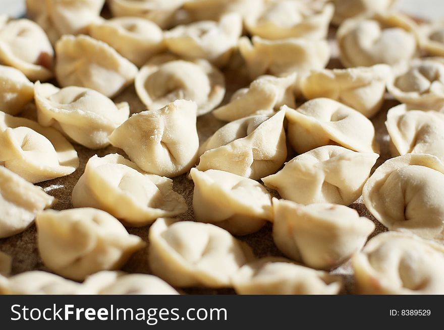 A lot of uncooked meat dumplings on kitchen preparation table