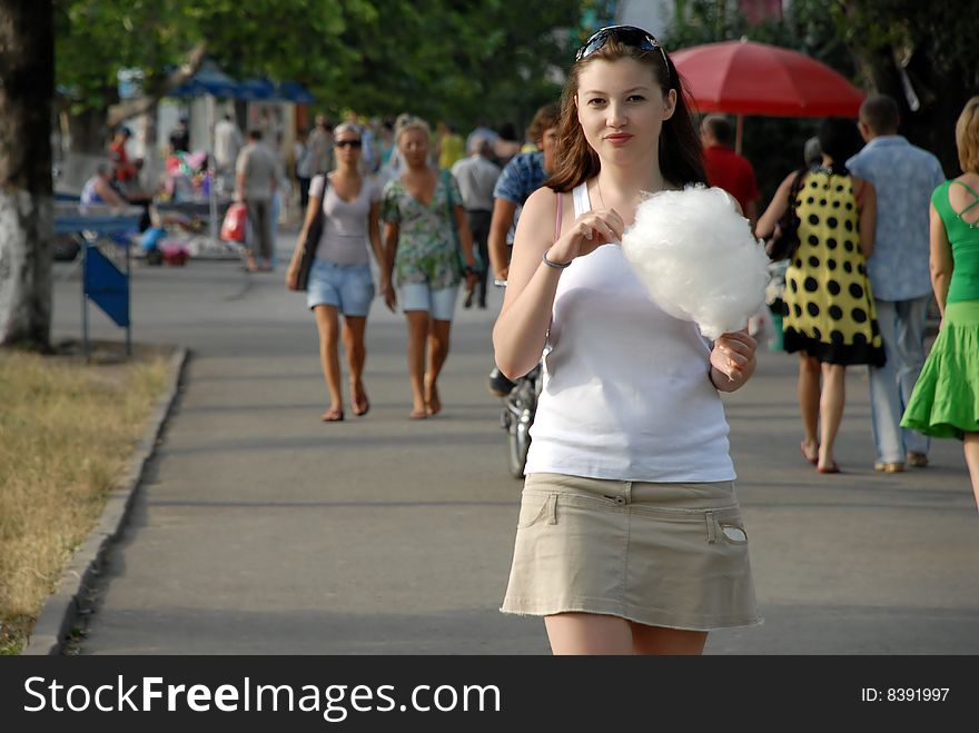 View of young woman eating cotton candy while walking in park.