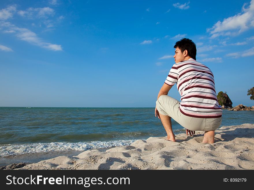 Squatting young man relaxing at the beach. Squatting young man relaxing at the beach