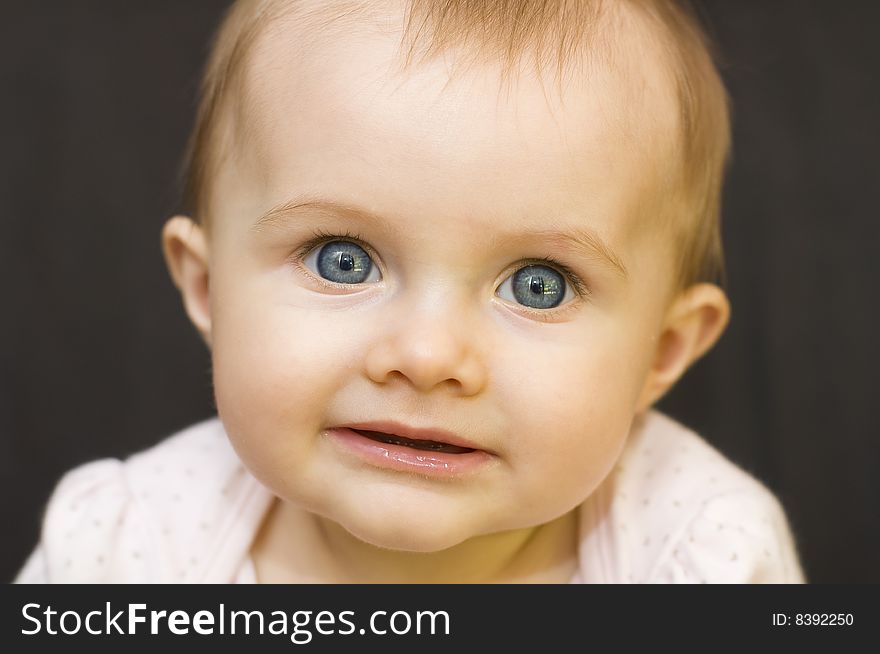 Portrait of a beautiful baby girl smiling and looking into the camera on a black background. Portrait of a beautiful baby girl smiling and looking into the camera on a black background