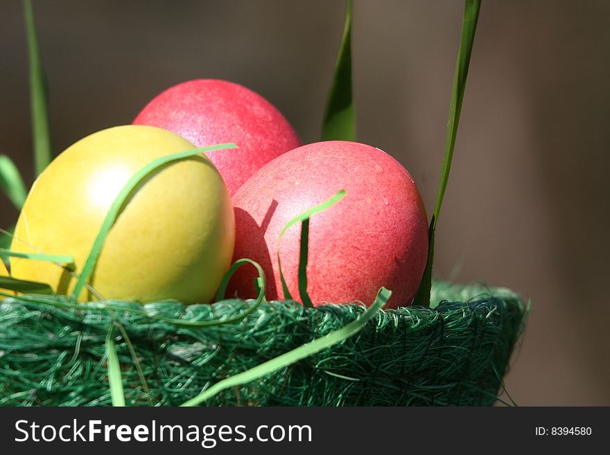 There is a green basket with easter bright yellow and pink eggs. There is a green basket with easter bright yellow and pink eggs.