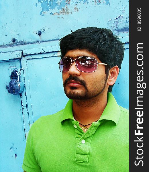 A stylish indian man with bright green t-shirt standing in front of a contrasting turquoise blue background