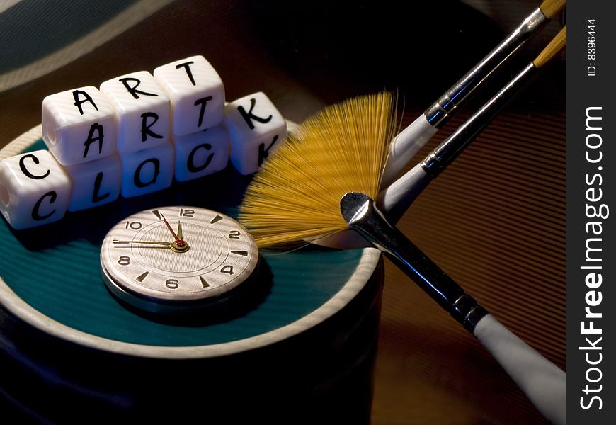 Abstract Composition. Reason inverted green cup with a broken bottom. From the hole sticking brush. In the inverted cup are hours and cubes. Cubes collected inscription ART CLOCK. Another brush rests on the cup. Dark background. Brushes with red hair. Abstract Composition. Reason inverted green cup with a broken bottom. From the hole sticking brush. In the inverted cup are hours and cubes. Cubes collected inscription ART CLOCK. Another brush rests on the cup. Dark background. Brushes with red hair.