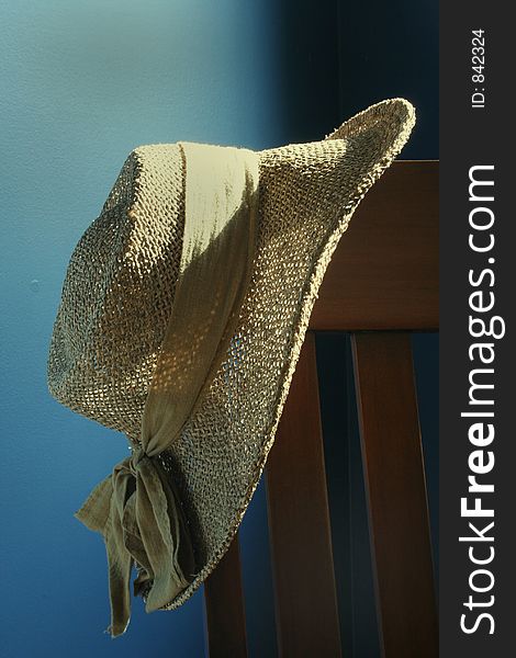 A straw hat hangs on a wooden chair. A straw hat hangs on a wooden chair