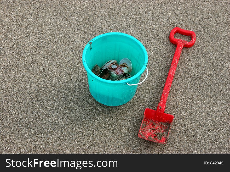 A red shovel on brownish sand and shells with space on its side to write or add text. A red shovel on brownish sand and shells with space on its side to write or add text.
