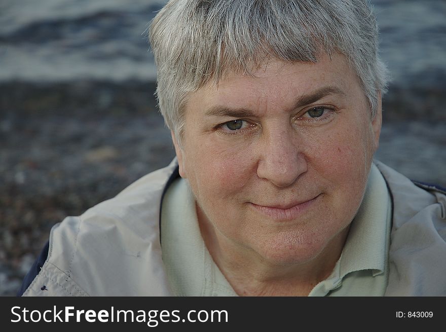 A portrait of a gray-haired woman with the lakeshore as a background.