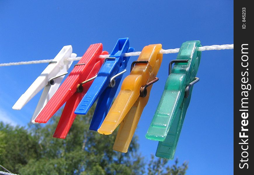 Clothespins in different colors on a clothesline against a blue sky. Clothespins in different colors on a clothesline against a blue sky