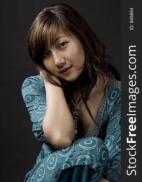 A beautiful young asian woman posing on a stool on black background. A beautiful young asian woman posing on a stool on black background