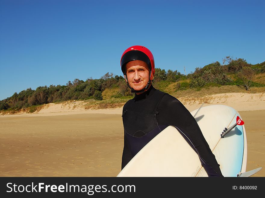 Physically fit and active senior with his board, wetsuit and helmet ready to go into the surf. Physically fit and active senior with his board, wetsuit and helmet ready to go into the surf