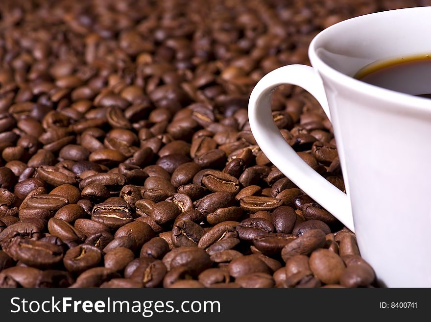 Shallow depth of field close-up of a freshly brewed cup of coffee on a bed of coffee beans. Shallow depth of field close-up of a freshly brewed cup of coffee on a bed of coffee beans