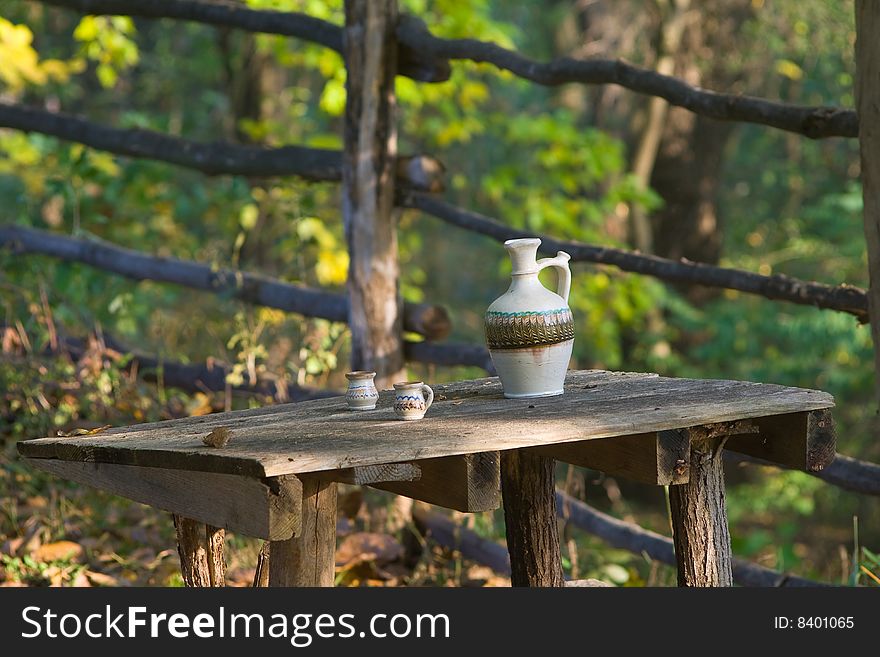 Rustic table wit water pot and two noggins in morning sunlight