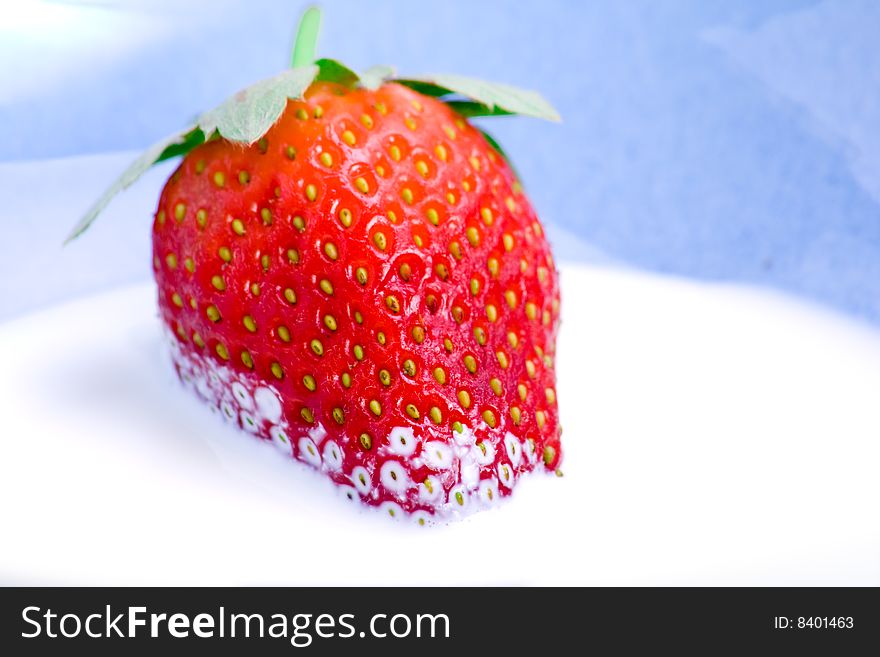 A fresh strawberry resting in a bowl of cream. A fresh strawberry resting in a bowl of cream