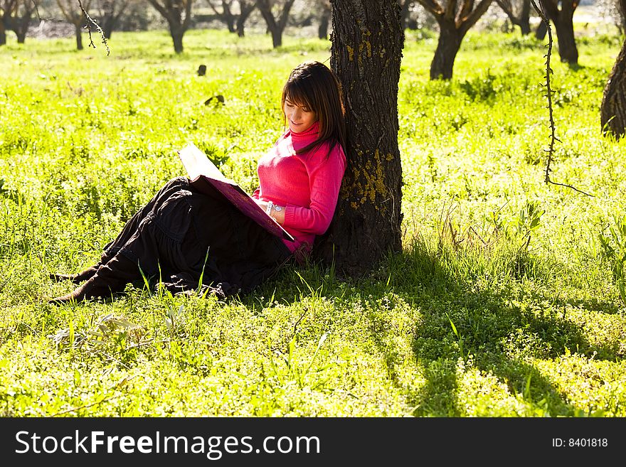 Young cheerful woman enjoying a book in the forest.