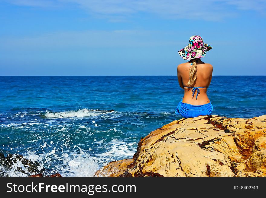 Girl in hat sitting on the rocks at the sea. Girl in hat sitting on the rocks at the sea