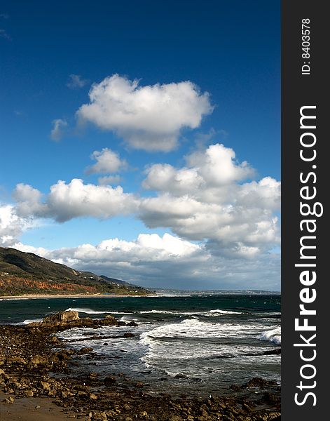 The rocky shore of Leo Carillo Beach in Southern California, with mountains in the background and white clouds in the sky. The rocky shore of Leo Carillo Beach in Southern California, with mountains in the background and white clouds in the sky