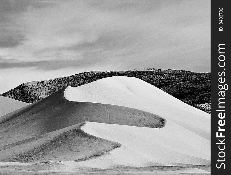 A tall and deeply textured sand dune stands in front of a mountain in the high desert of Nevada. A tall and deeply textured sand dune stands in front of a mountain in the high desert of Nevada