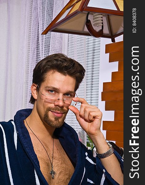 Young man wearing blue striped bathrobe puts on his glasses. Young man wearing blue striped bathrobe puts on his glasses